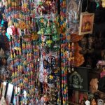 A vibrant display of colorful hanging ornaments and bells is showcased alongside various decorative items and framed pictures in a shop. The assortment includes beads, intricate patterns, and idols, creating a visually rich and eclectic ambiance.