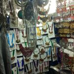 A display of various colorful, traditional jewelry sets hanging on a wall in a shop. The sets include necklaces, earrings, and other accessories, often adorned with beads, stones, and intricate designs. The vibrant colors and patterns make the display visually striking.